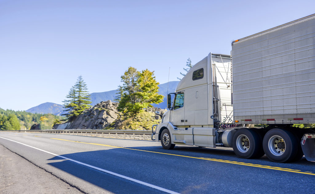 Big rig white bonnet long haul semi truck transporting frozen food in refrigerator semi trailer running on the road in Columbia Gorge